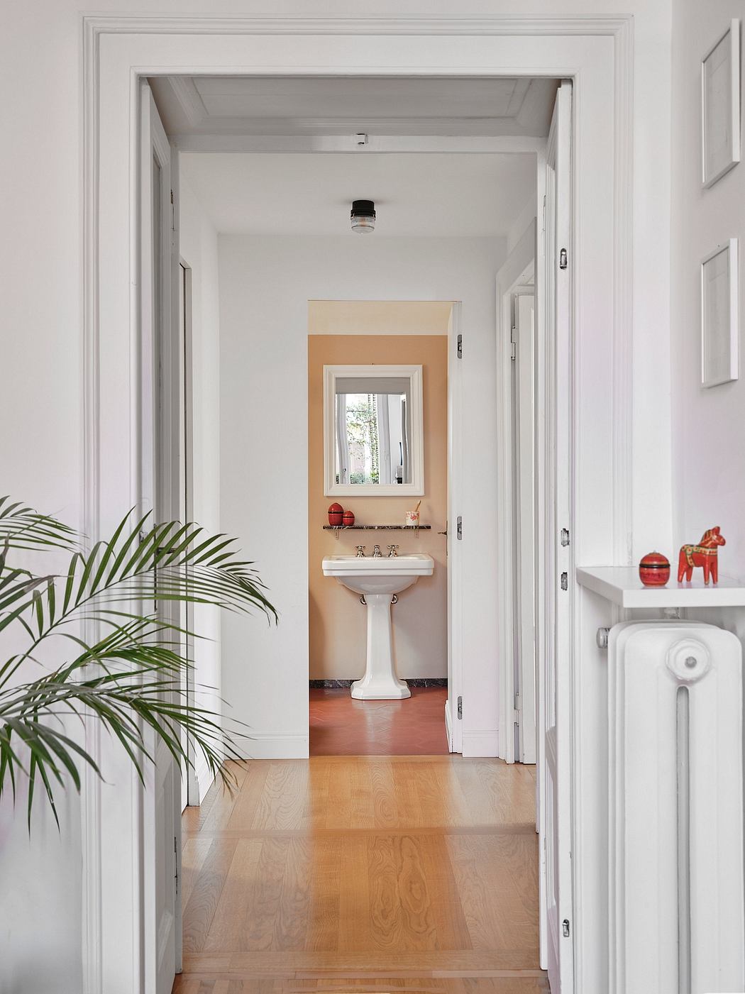 Bright, minimalist hallway with white walls, hardwood floors, and a pedestal sink framed by a window.