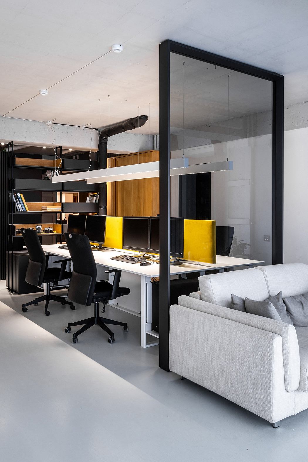 A modern office space with glass partitions, black desks, and a cozy gray sofa.