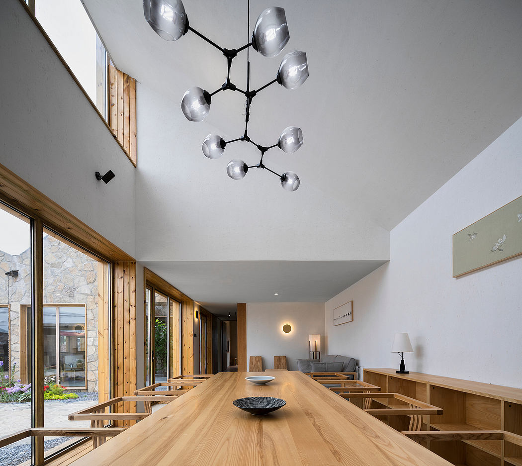 Sleek modern chandelier suspended over a large wooden dining table in a spacious room.
