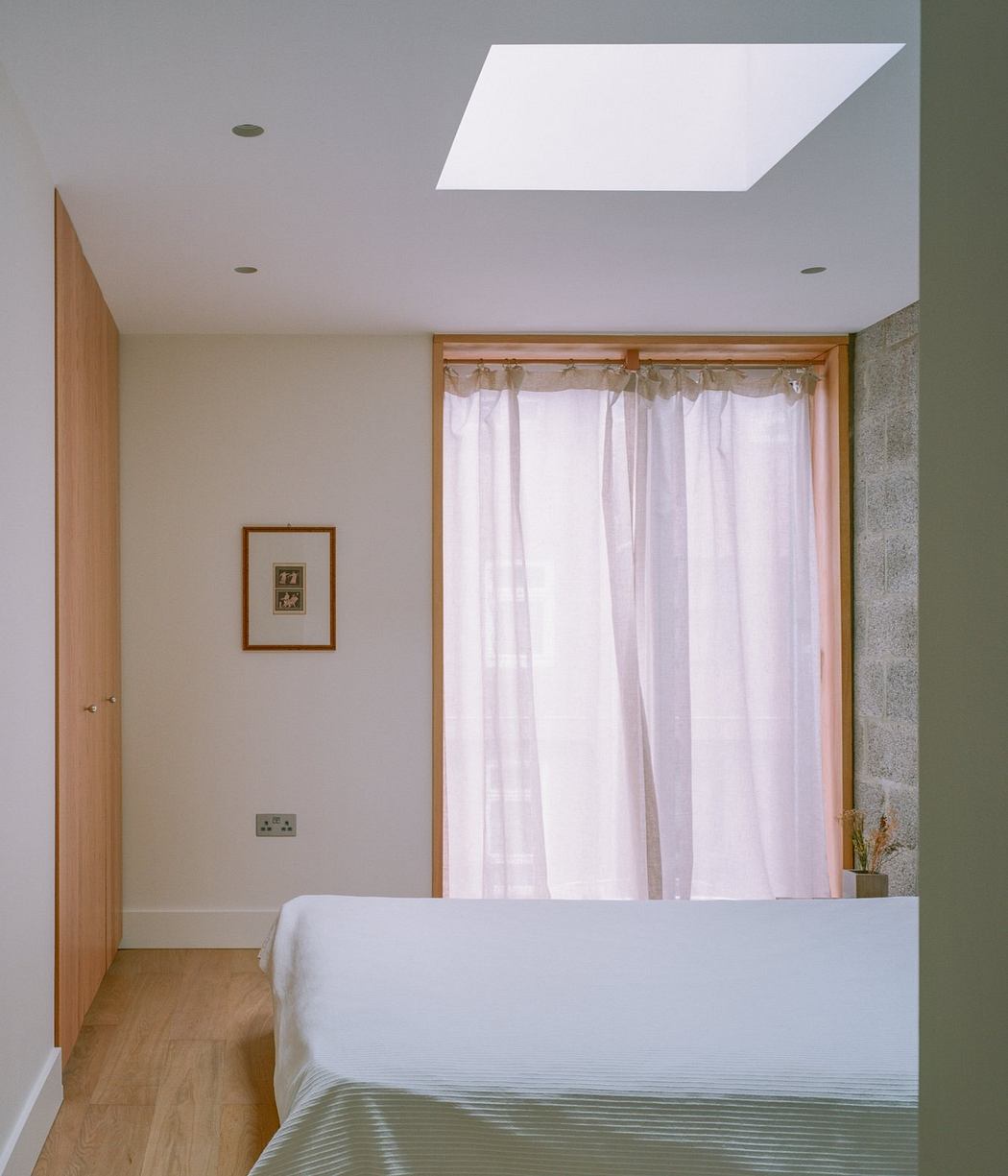 Minimalist bedroom with wooden framing, white curtains, and a skylight above the bed.