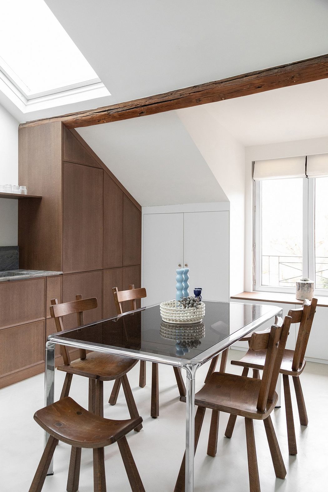 Bright, minimalist kitchen with wood beams, modern glass dining table, and rustic chairs.