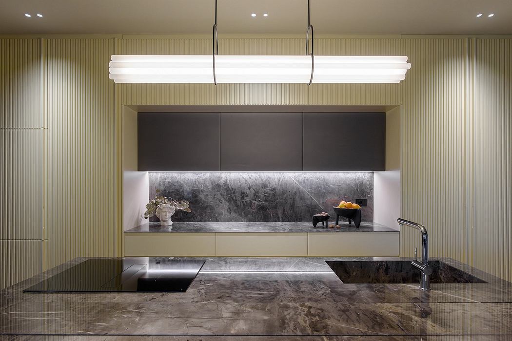 A sleek, modern kitchen with a linear lighting fixture, dark cabinetry, and a marble countertop.