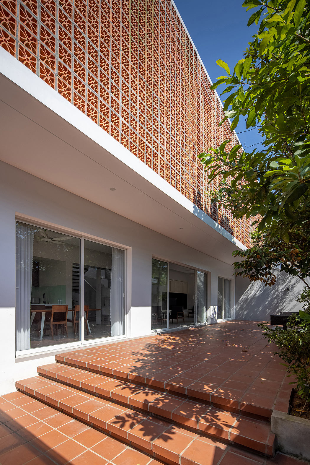 A modern architectural facade with intricate brick lattice and a tiled terrace overlooking greenery.
