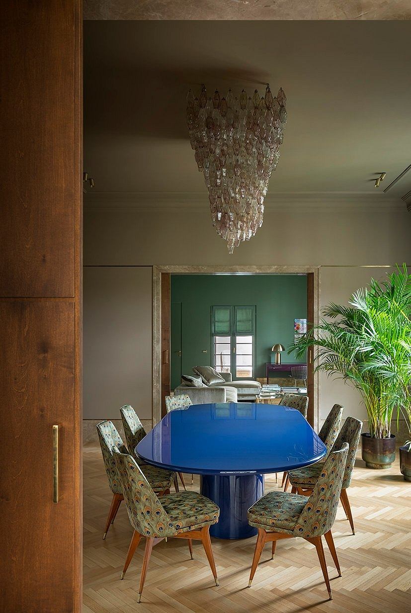 A stunning dining room with a vibrant blue circular table, patterned chairs, and an ornate crystal chandelier.