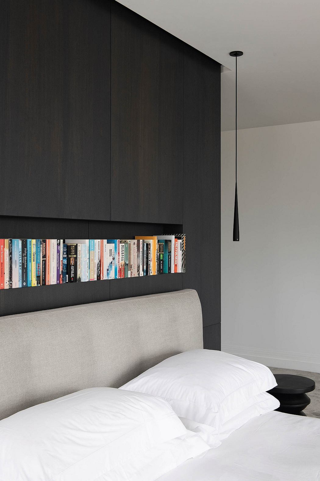 Minimalist bedroom design with built-in bookshelf, pendant light, and upholstered headboard.