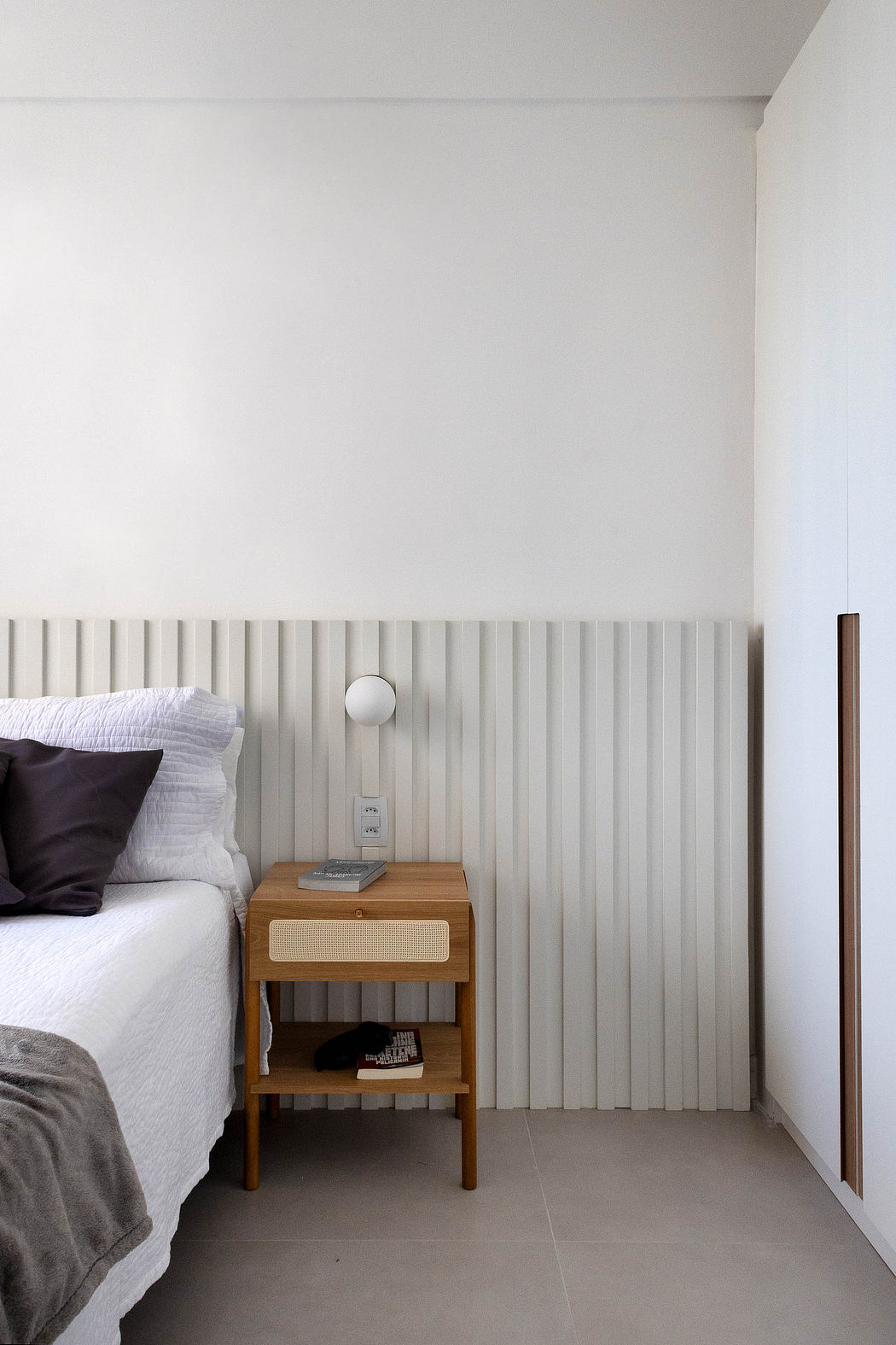 Minimalist bedroom design with vertical wood paneling, bedside table, and speaker.