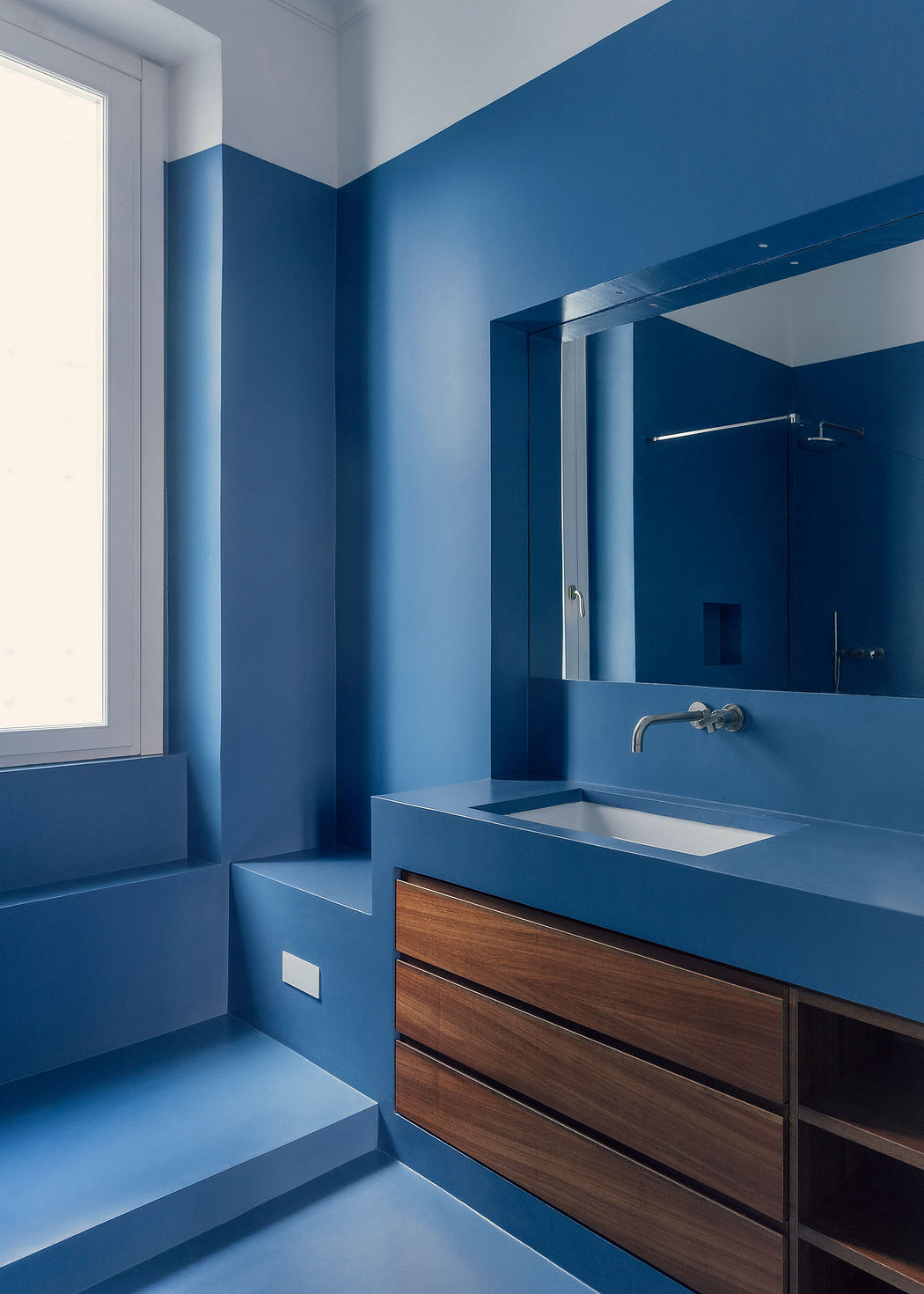 A modern bathroom with blue tiled walls, wooden vanity, and a wall-mounted sink.