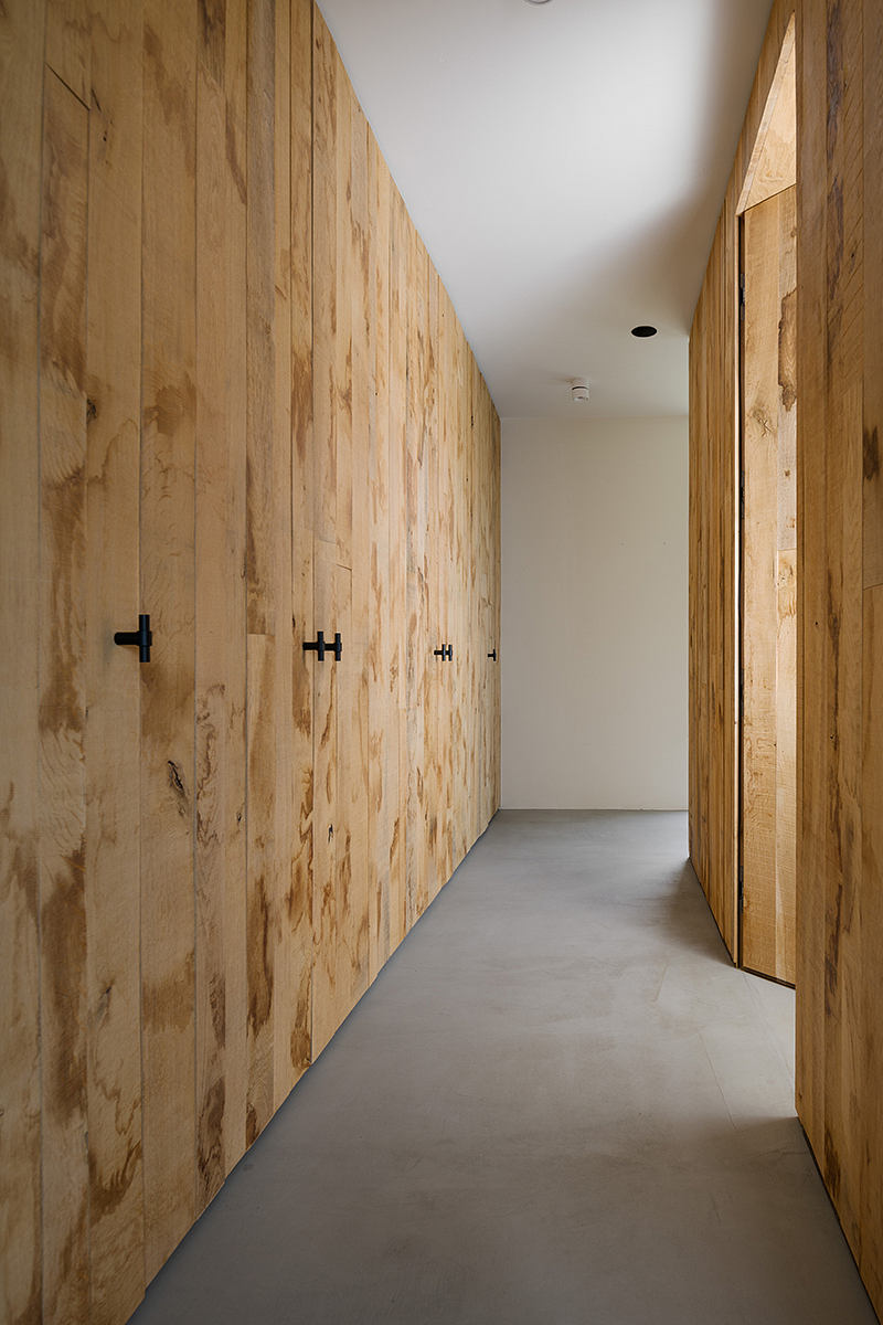 A minimalist, wood-paneled hallway with concrete flooring and recessed lighting.