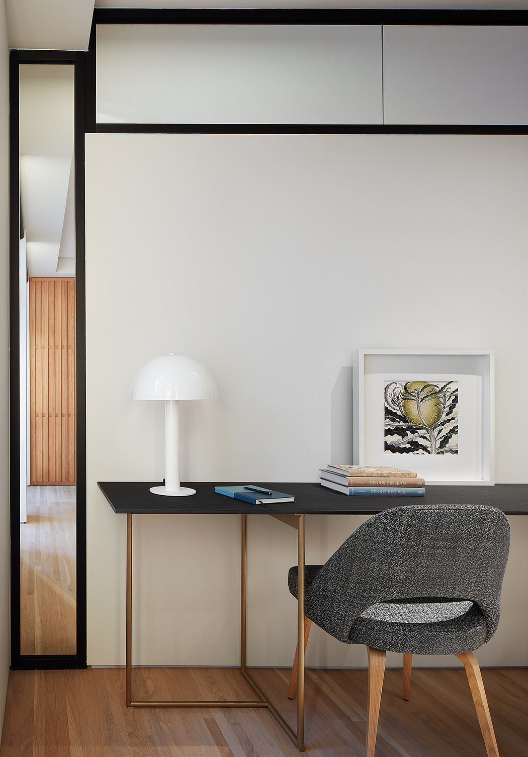 Minimalist workspace with sleek desk, modern lamp, and artwork against white wall.