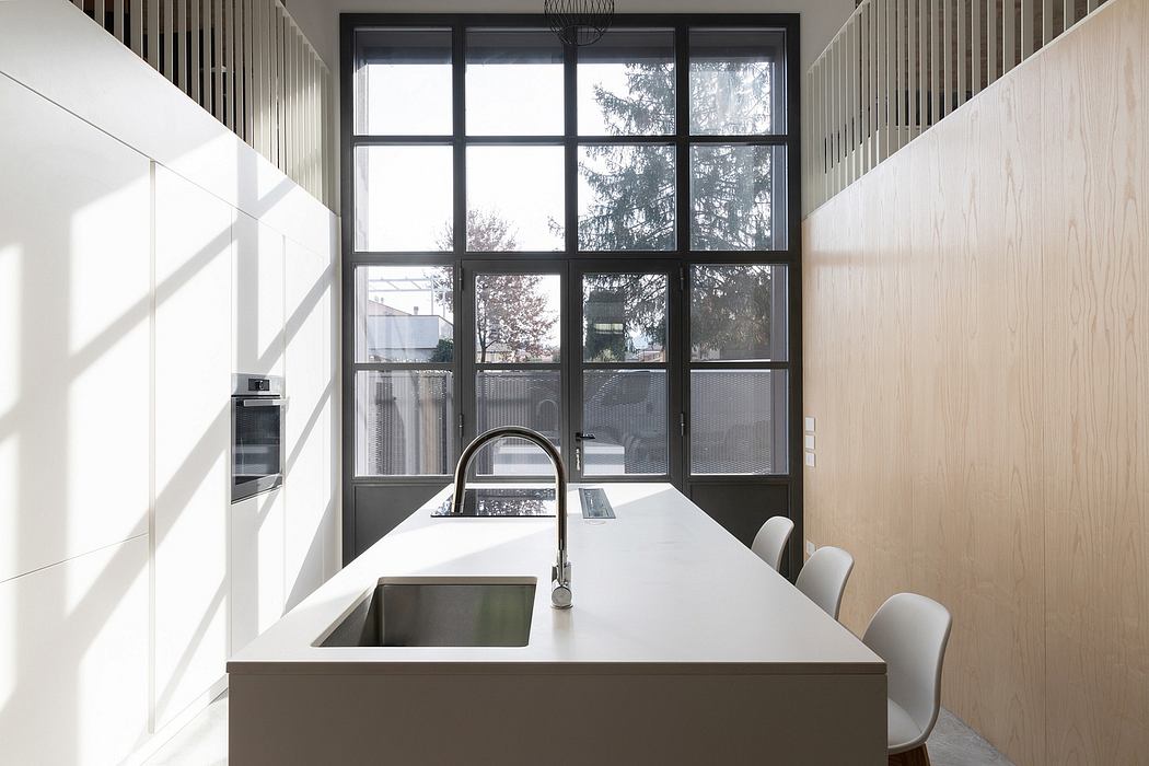 A modern, minimalist kitchen with large windows, sleek white countertops, and black steel frames.