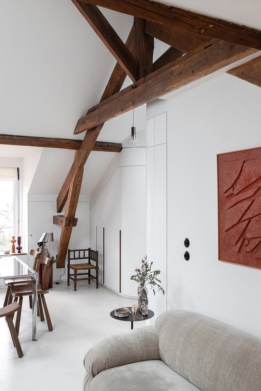 Cozy attic living space with exposed wooden beams, contemporary furnishings, and artwork.