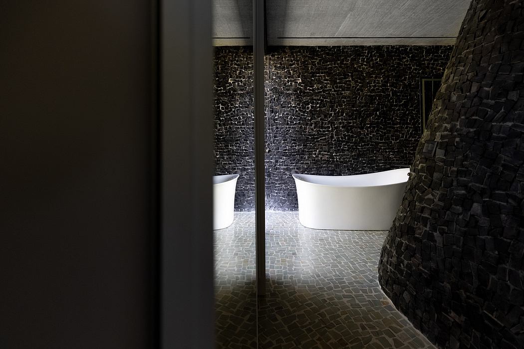 Dramatic stone walls and stark white bathtubs create a moody, modern bathroom setting.