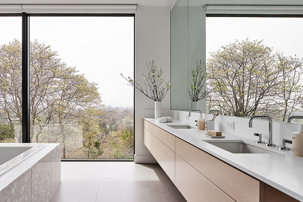 Spacious, minimalist bathroom with large windows overlooking a lush, forested landscape.