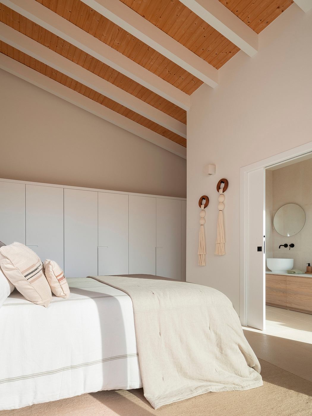 Warm, cozy bedroom with a striking exposed wooden ceiling, built-in cabinets, and a round mirror.