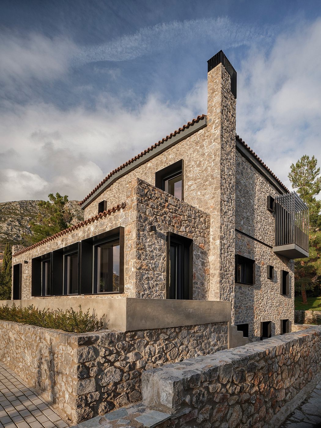 A stone and concrete modernist structure with a sloped roof, tall chimney, and expansive windows.