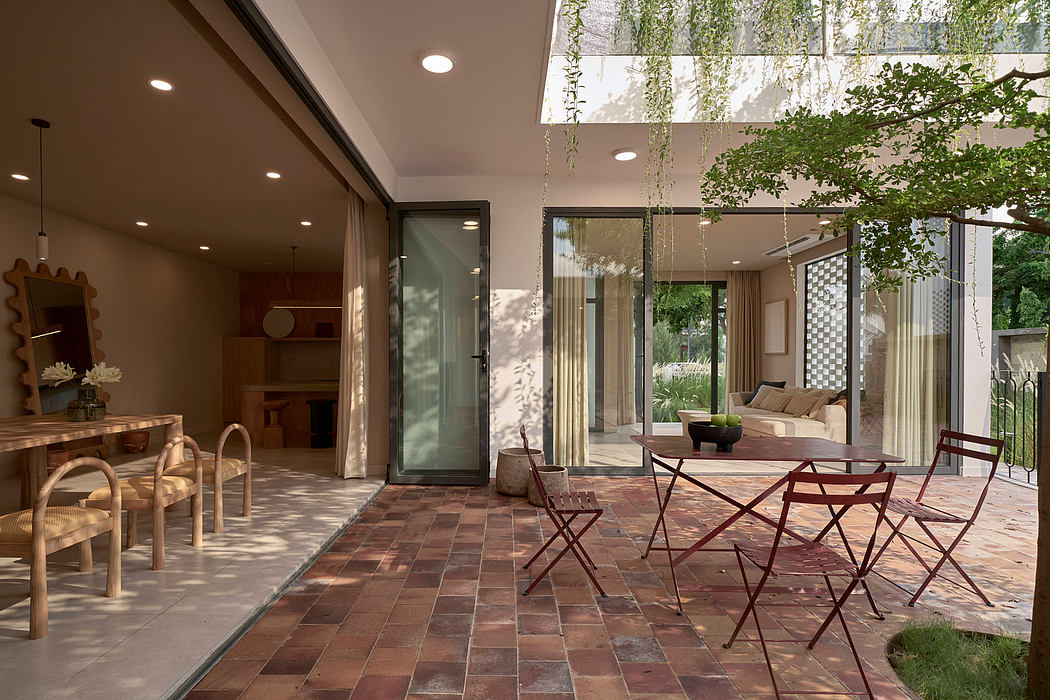 Striking glass doors open to a lush, modern outdoor patio with tiled flooring and furnishings.