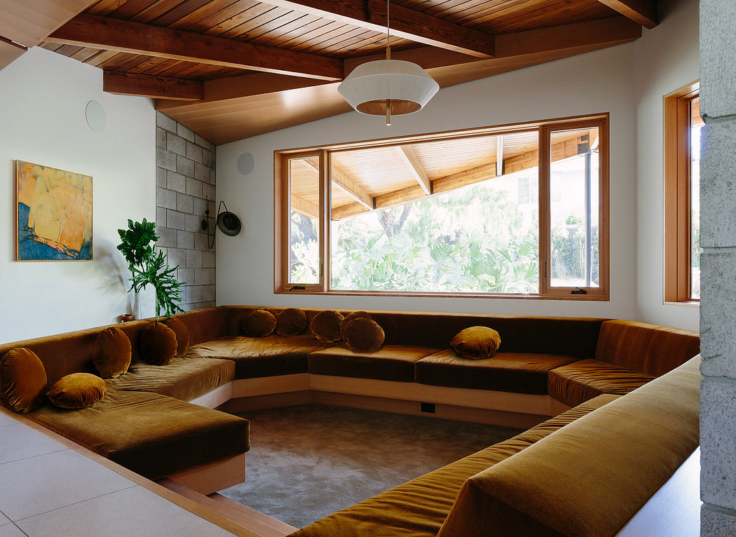 A cozy living room with a large, comfortable sectional sofa, wooden beamed ceiling, and expansive windows overlooking nature.