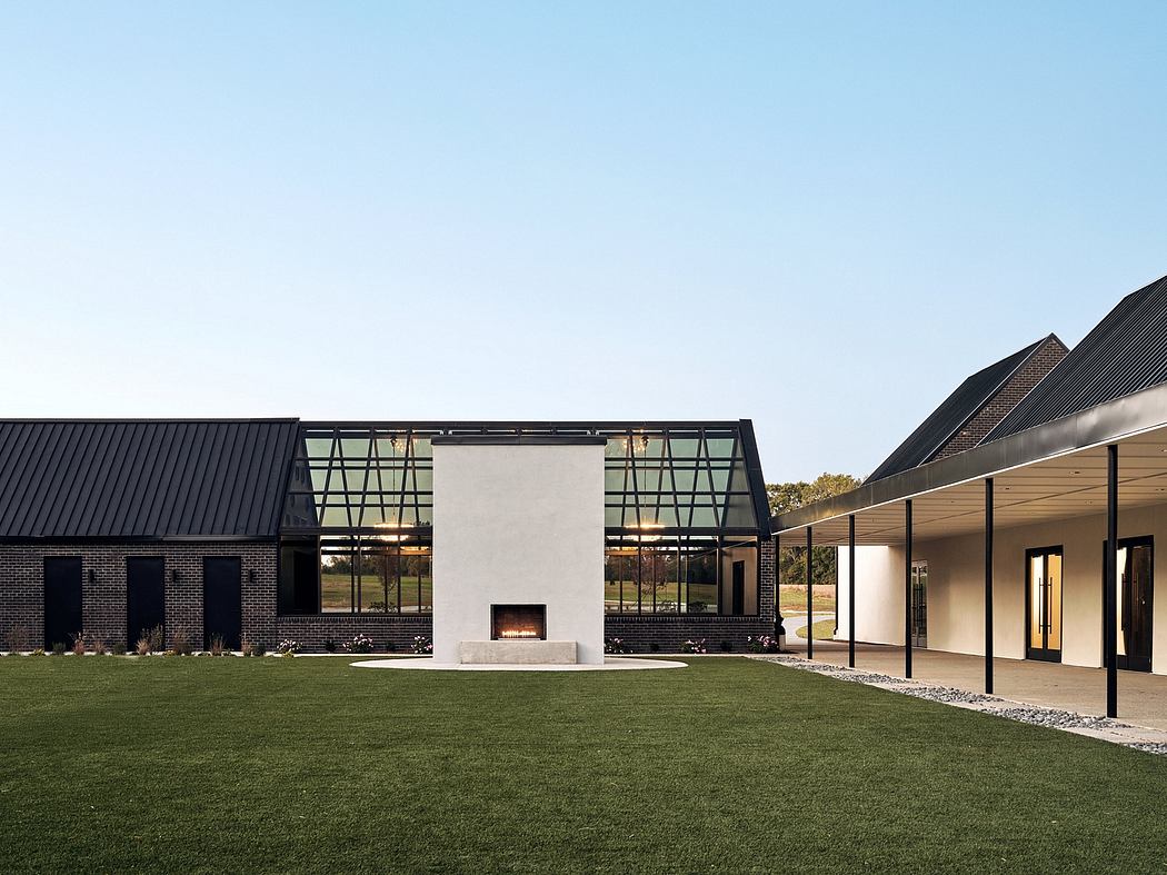 A modern, minimalist building with a large central fireplace, glass walls, and a grassy lawn.