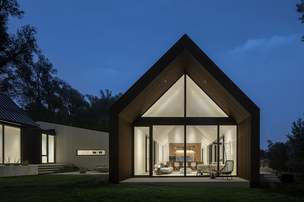 Modern A-frame home with wooden exterior, large windows, and a cozy interior visible at night.