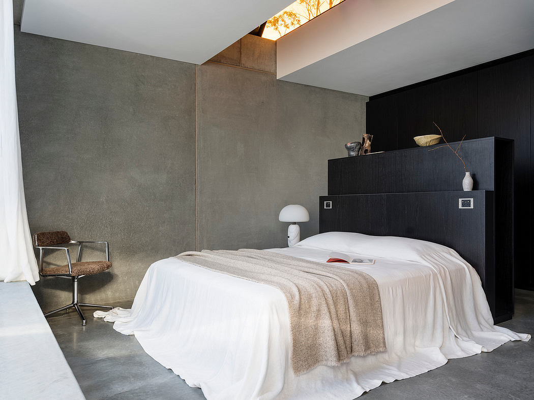 A modern, minimalist bedroom with concrete walls, a large black headboard, and simple decor.