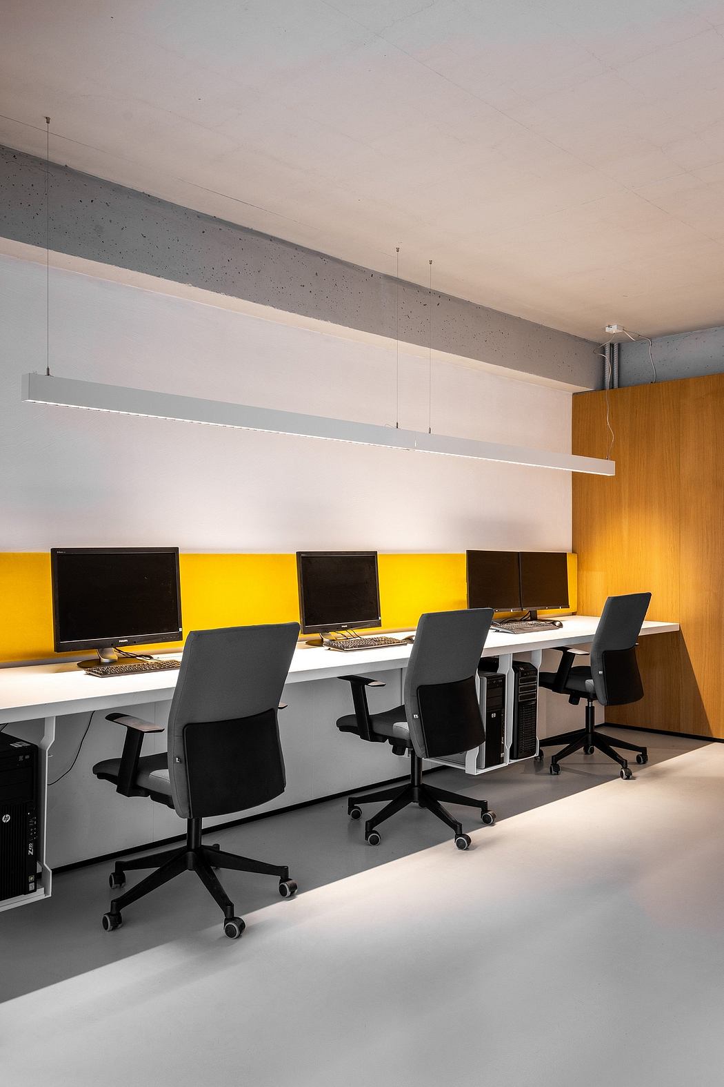 A modern office space with gray concrete walls, yellow accents, and sleek workstations.