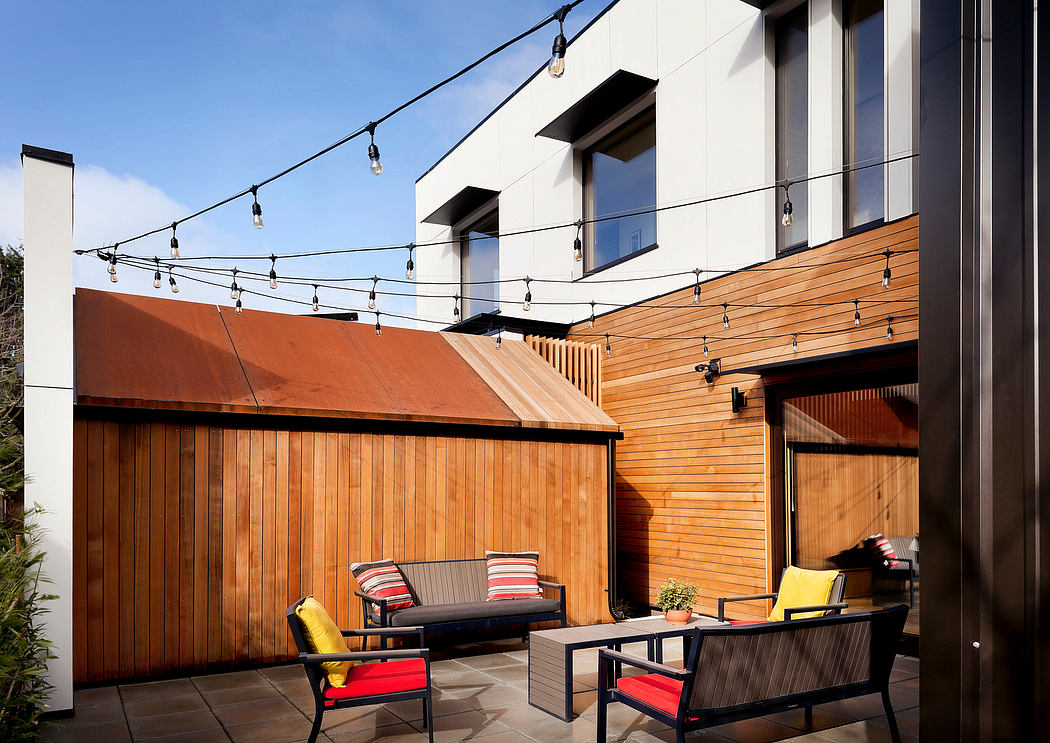 Sleek modern outdoor patio with wood siding, string lights, and minimalist furniture.