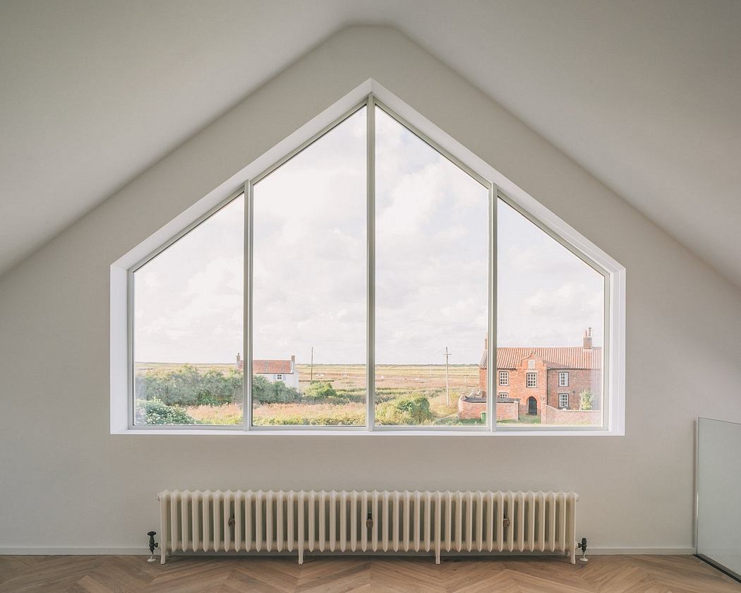 Triangular window overlooking brick buildings and rural landscape, with a radiator below.