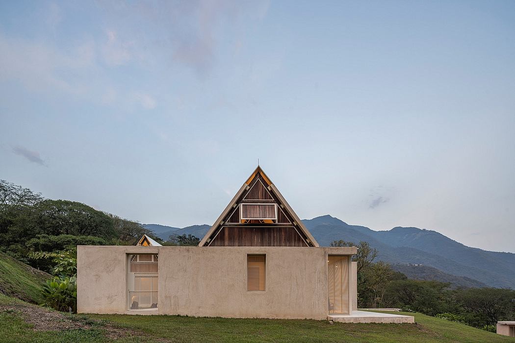 A triangular-roofed structure with wooden and concrete elements, nestled in a lush, mountainous landscape.