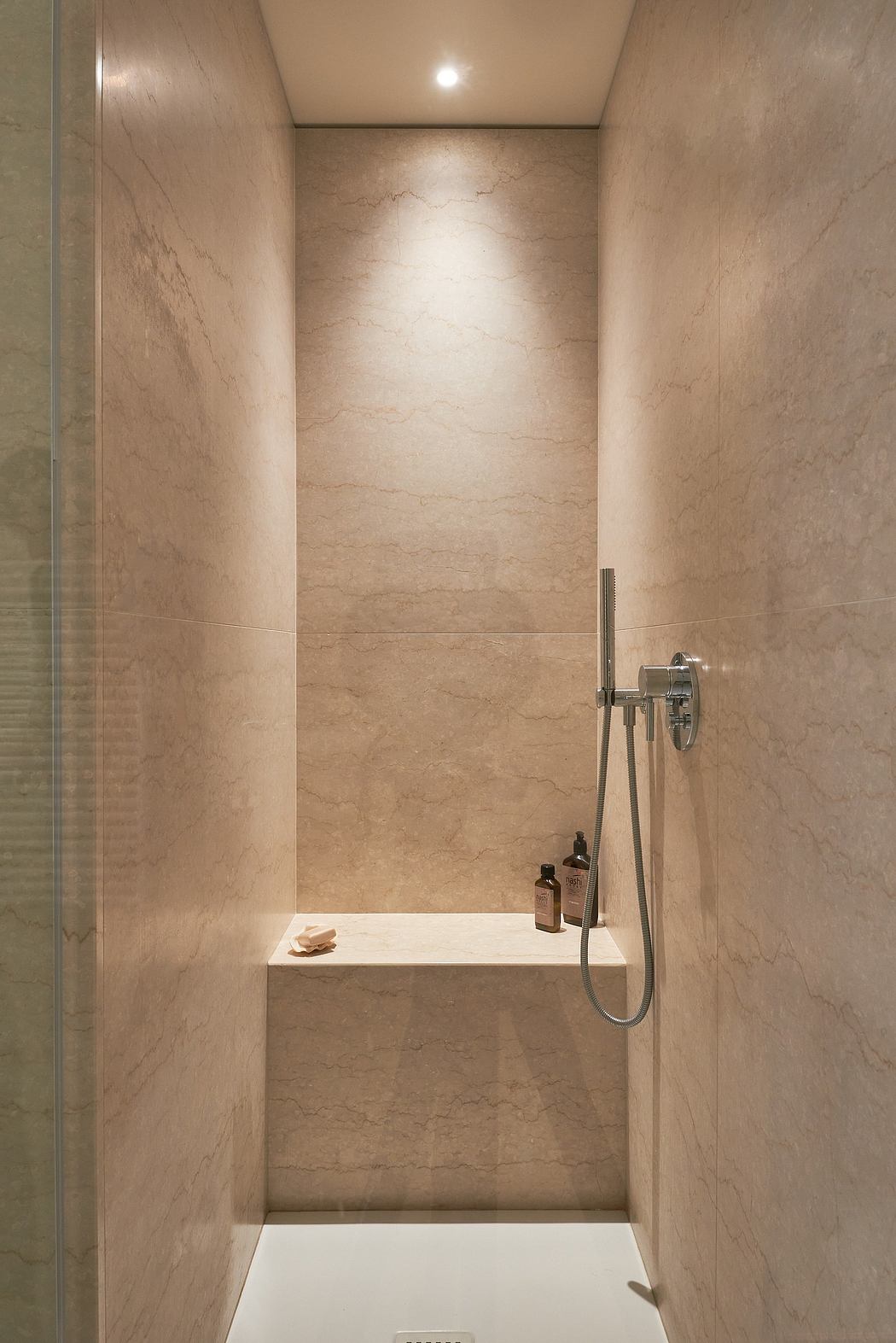 A minimalist, marble-clad shower stall with a recessed niche and a handheld shower head.