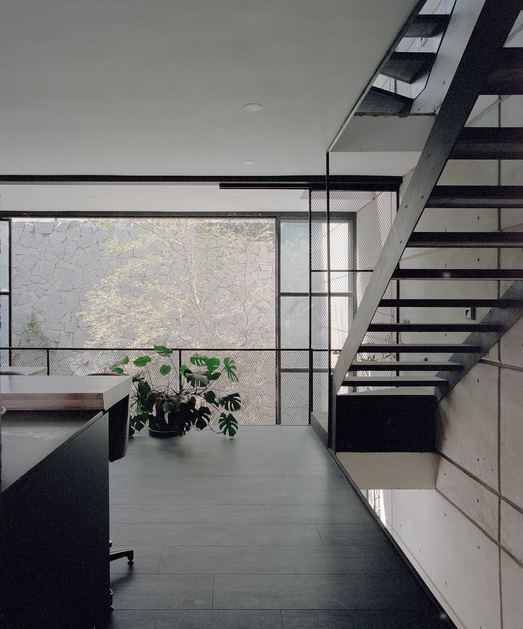 Modern, minimalist interior with large windows overlooking trees, black metal stairs, and potted plants.
