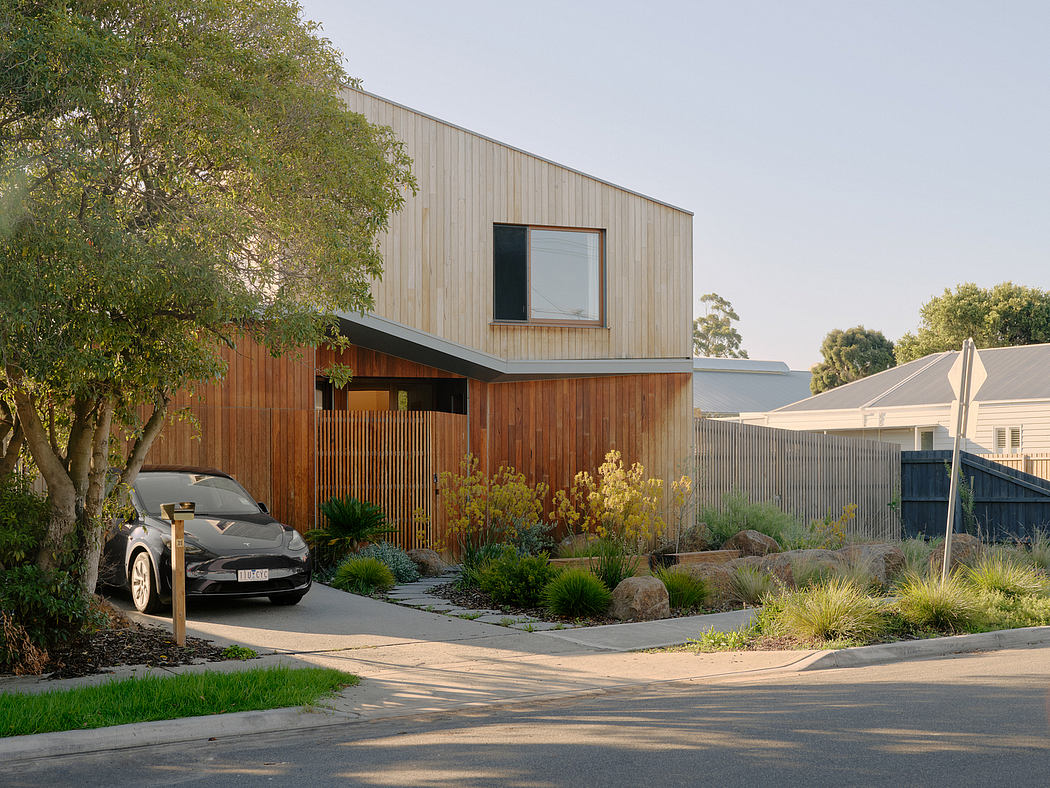 A modern, wood-clad home with an electric vehicle parked in a landscaped driveway.