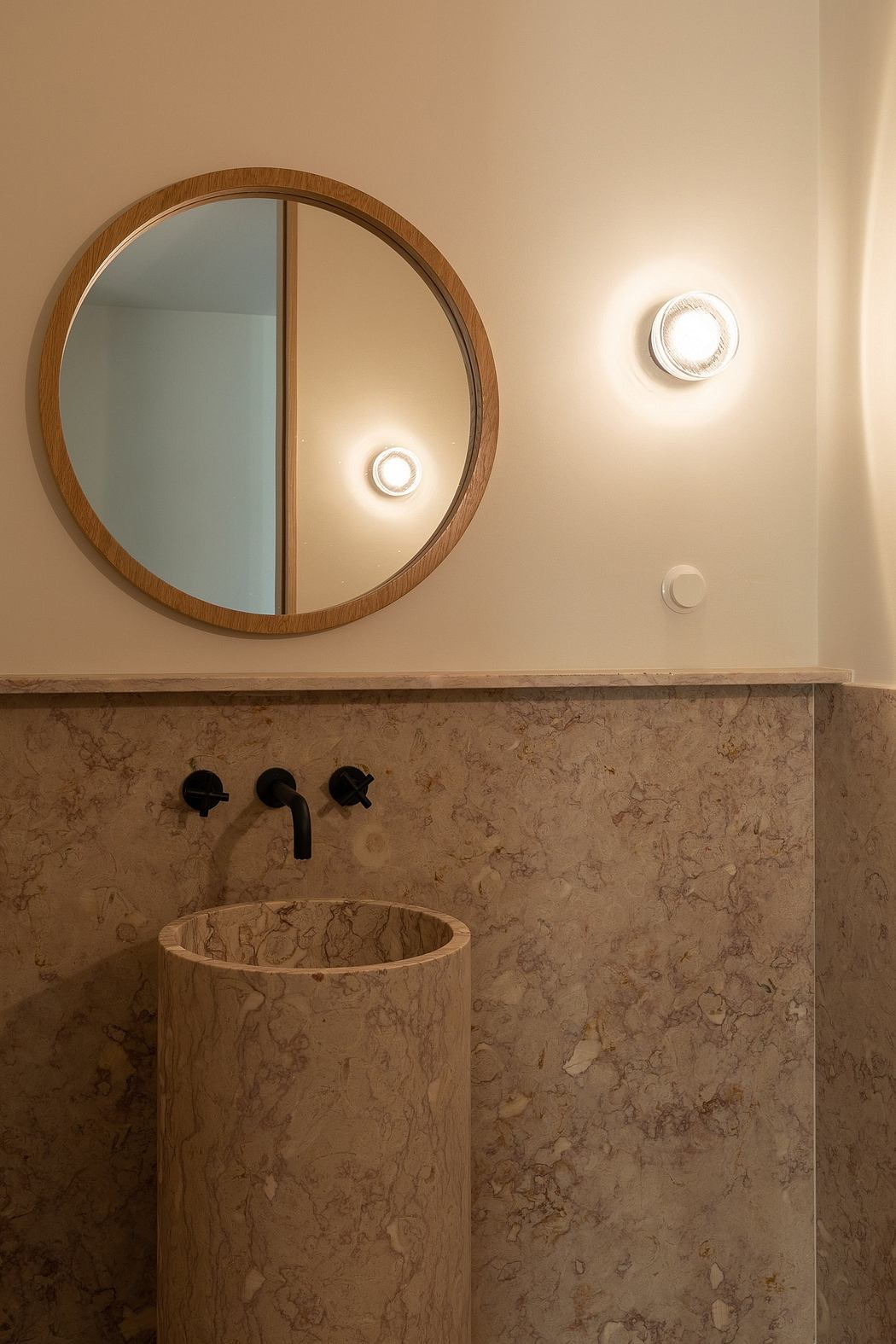 Circular wooden-framed mirror above a stone vanity with black fixtures and accent lighting.