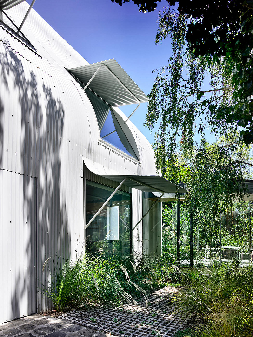 Modern architectural design featuring angular, metal-clad building with lush, natural landscaping.