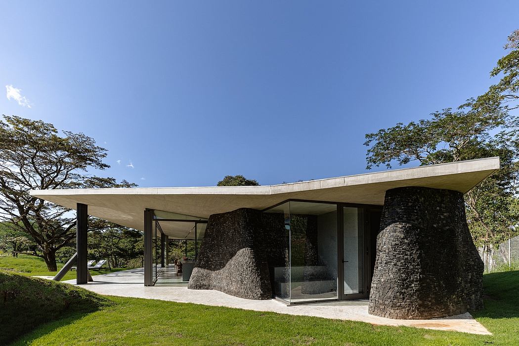 Modern concrete and stone structure with glass walls surrounded by lush greenery.