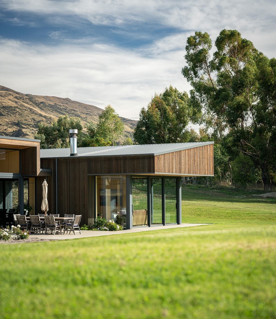 A modern, wooden-clad structure nestled in a lush, grassy landscape with mountains in the background.