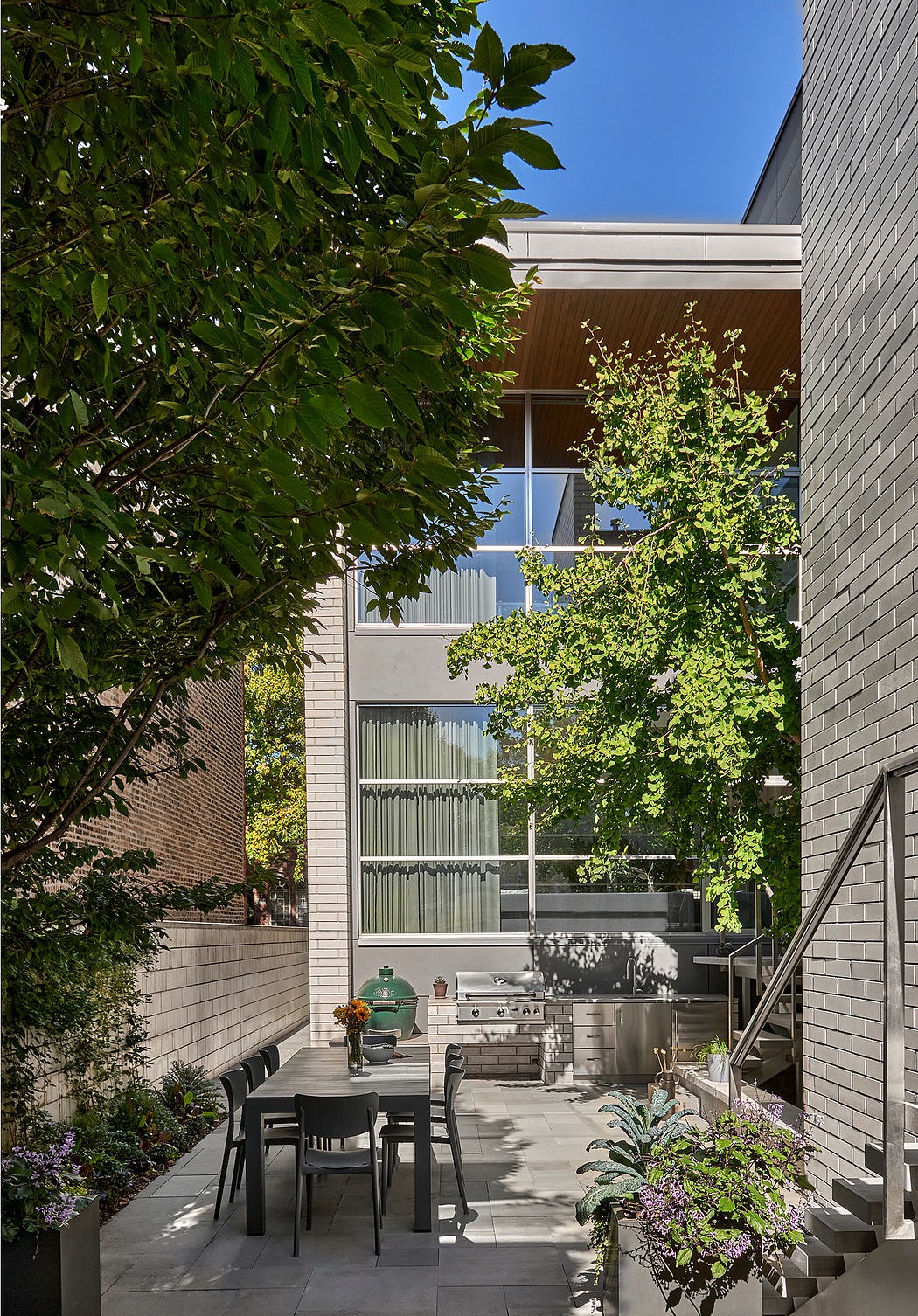 Outdoor patio with modern architecture, greenery, and a built-in grill area.