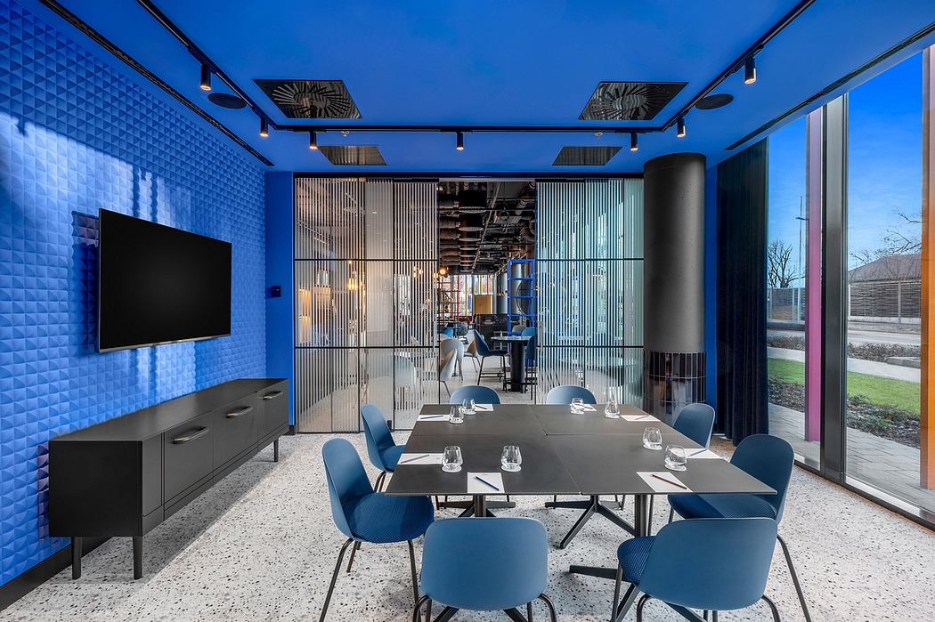 Modern conference room with geometric blue walls, sleek furniture, and large windows overlooking greenery.