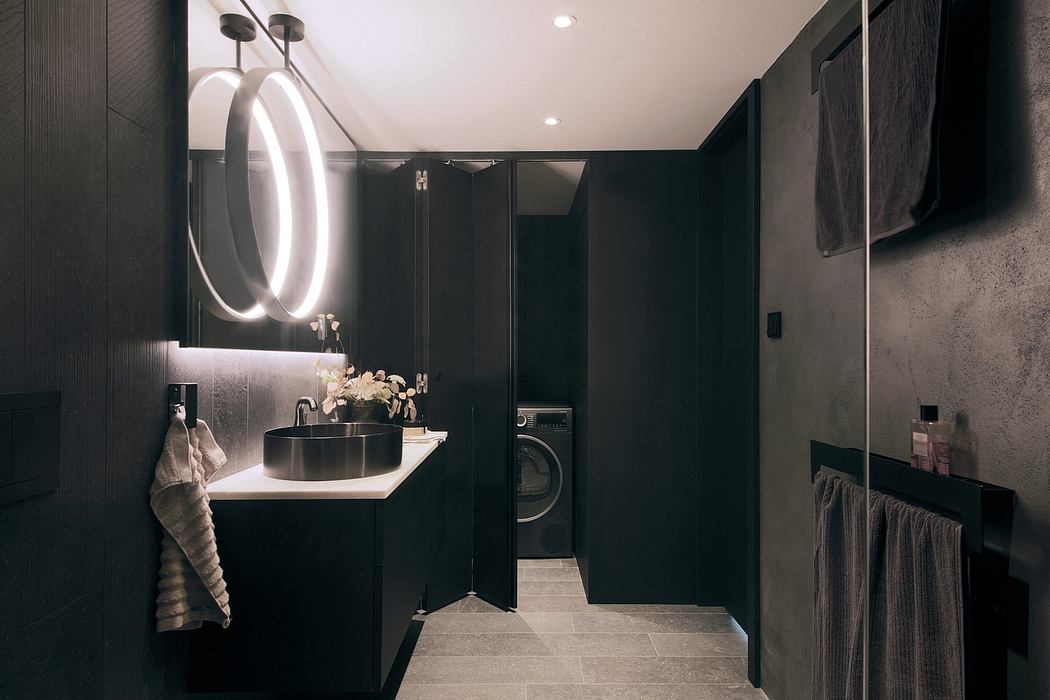 Sleek, modern bathroom with dark cabinetry, round lit mirror, and integrated washer.