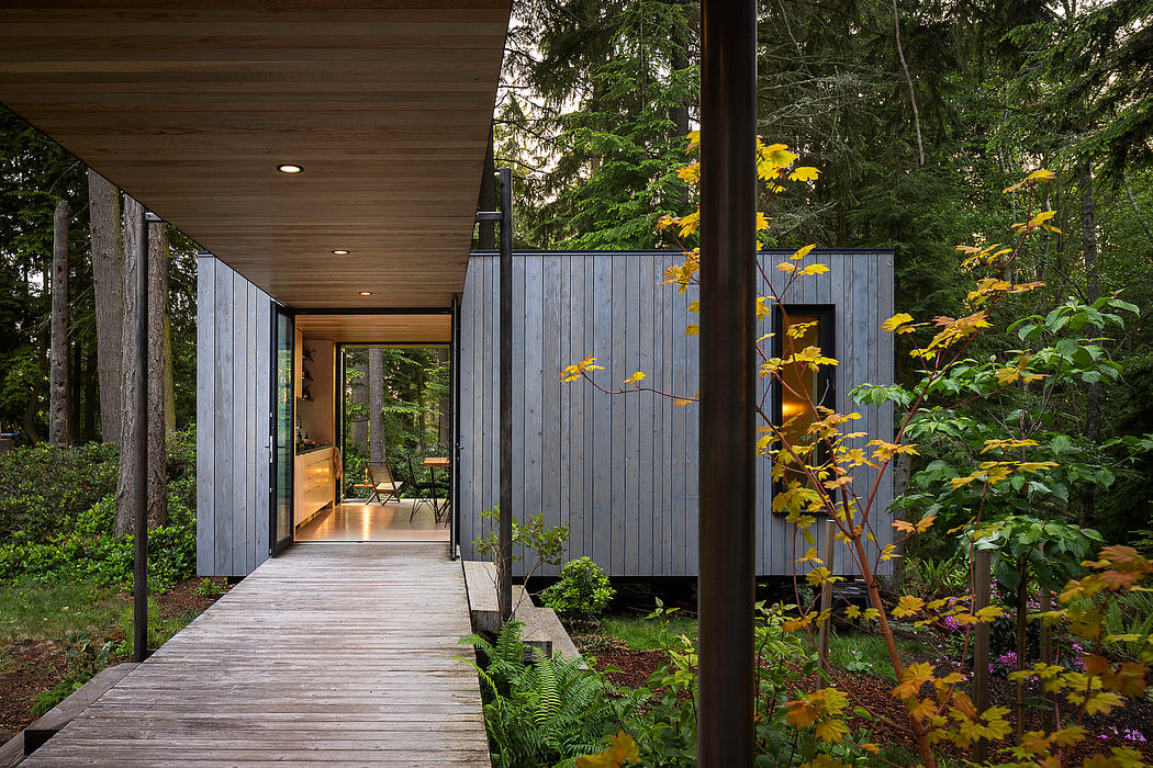 A modern, wooden-exterior cabin nestled in a lush, forested environment with a covered walkway.