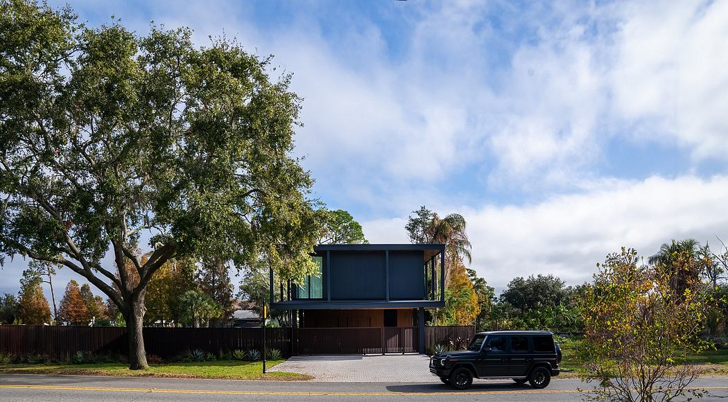 Modern, two-story house with clean lines, dark exterior, and large trees surrounding the property.