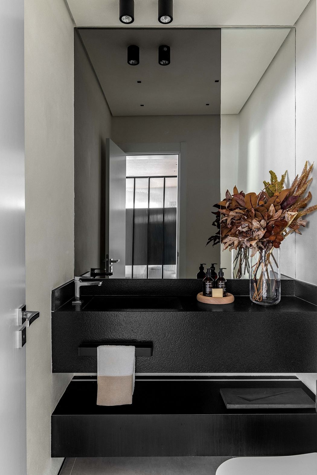 Sleek, minimalist bathroom design with black countertop, recessed lighting, and fall-themed floral arrangement.