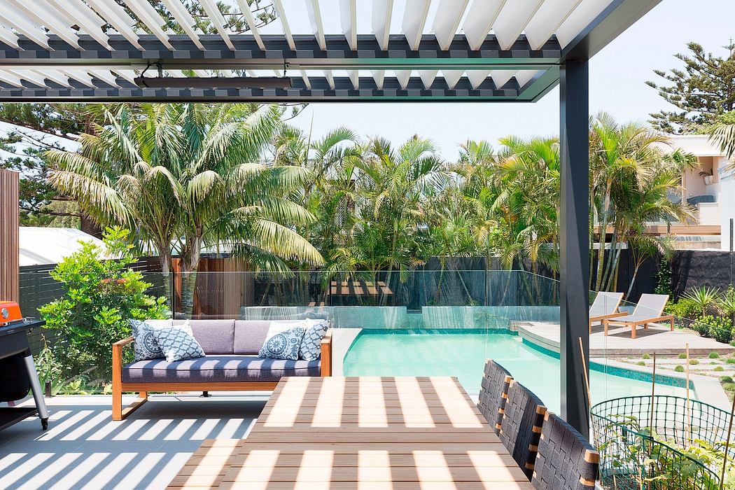A modern, open-concept outdoor living space with a pool, wooden deck, and lush tropical foliage.