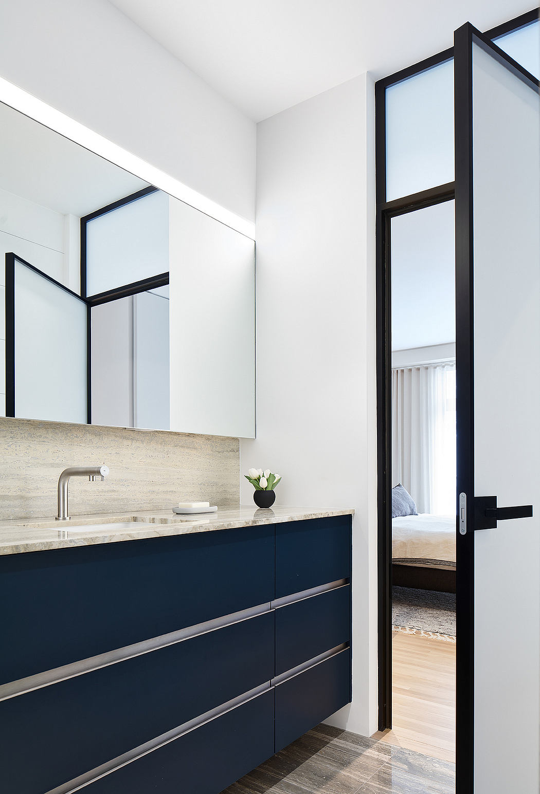 Modern bathroom vanity with sleek, black drawers and a light granite countertop. Frameless mirror and glass walls create an airy, minimalist aesthetic.