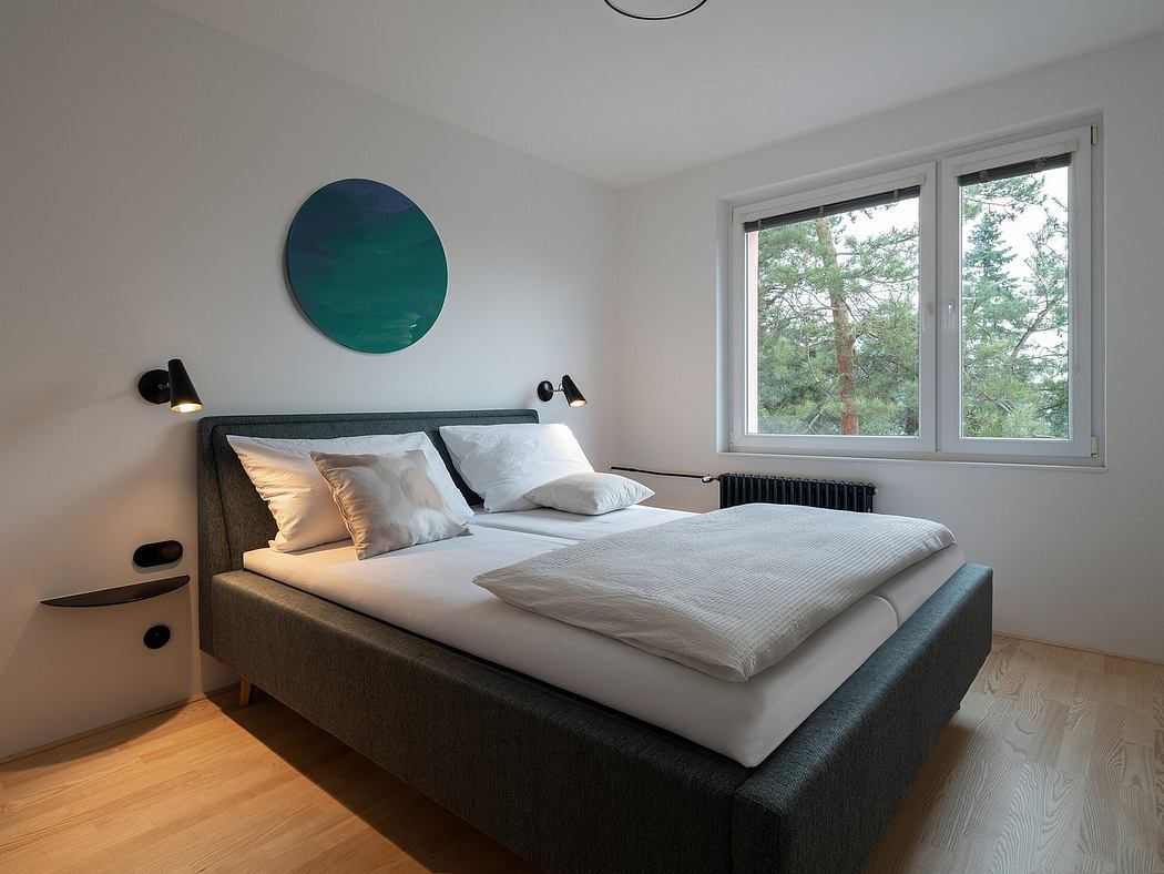 Minimalist bedroom with large circular artwork, black bed frame, and views of forest.