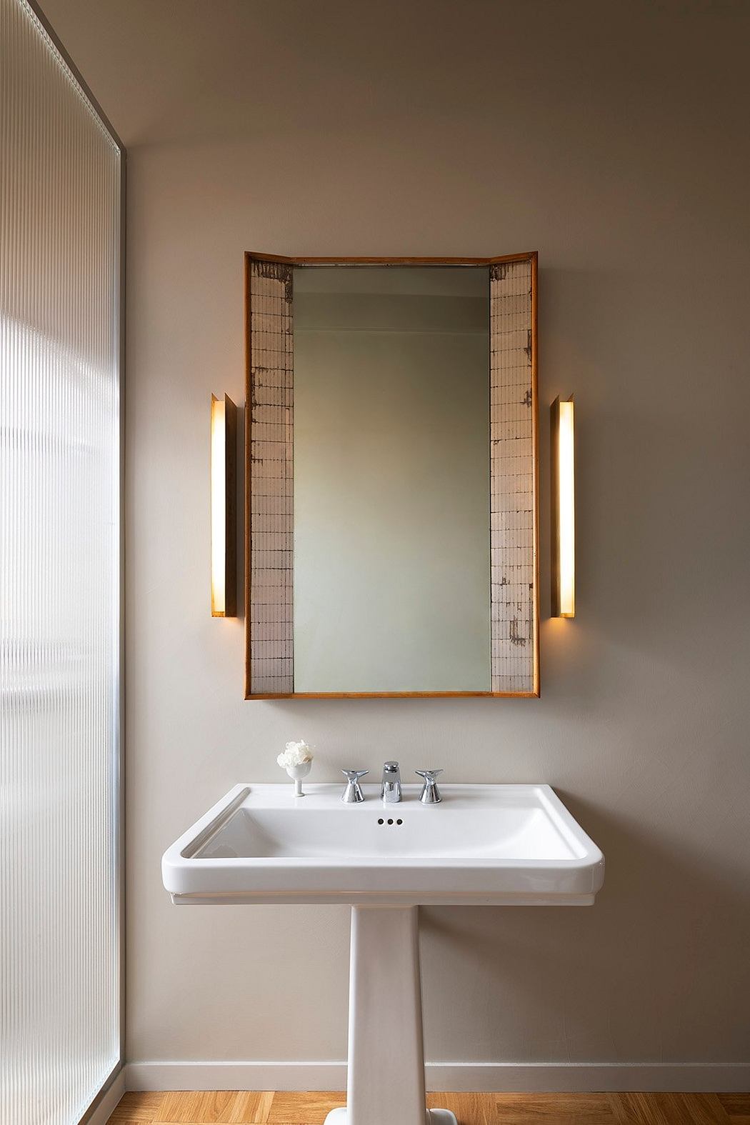 A modern bathroom with a framed mirror, sconce lighting, and a white pedestal sink.