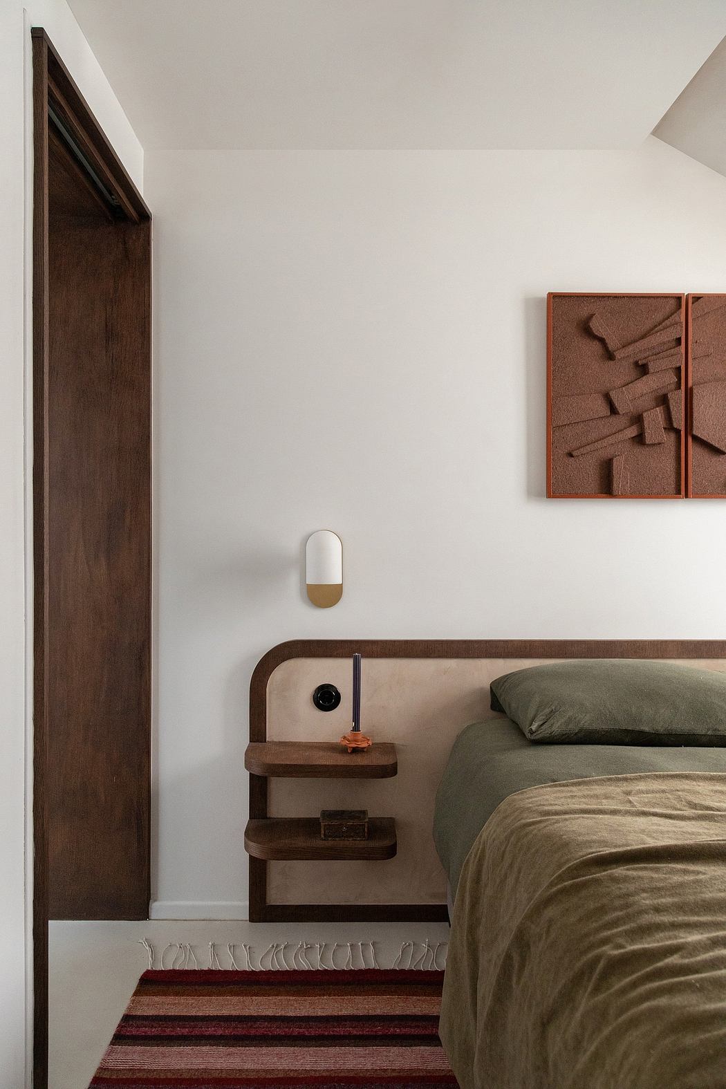 Minimalist bedroom with dark wooden accents, textured wall art, and built-in nightstand.