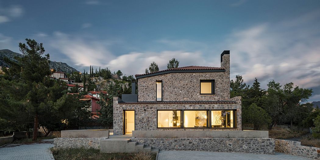 Two-story stone house with large windows overlooking a mountainous landscape.