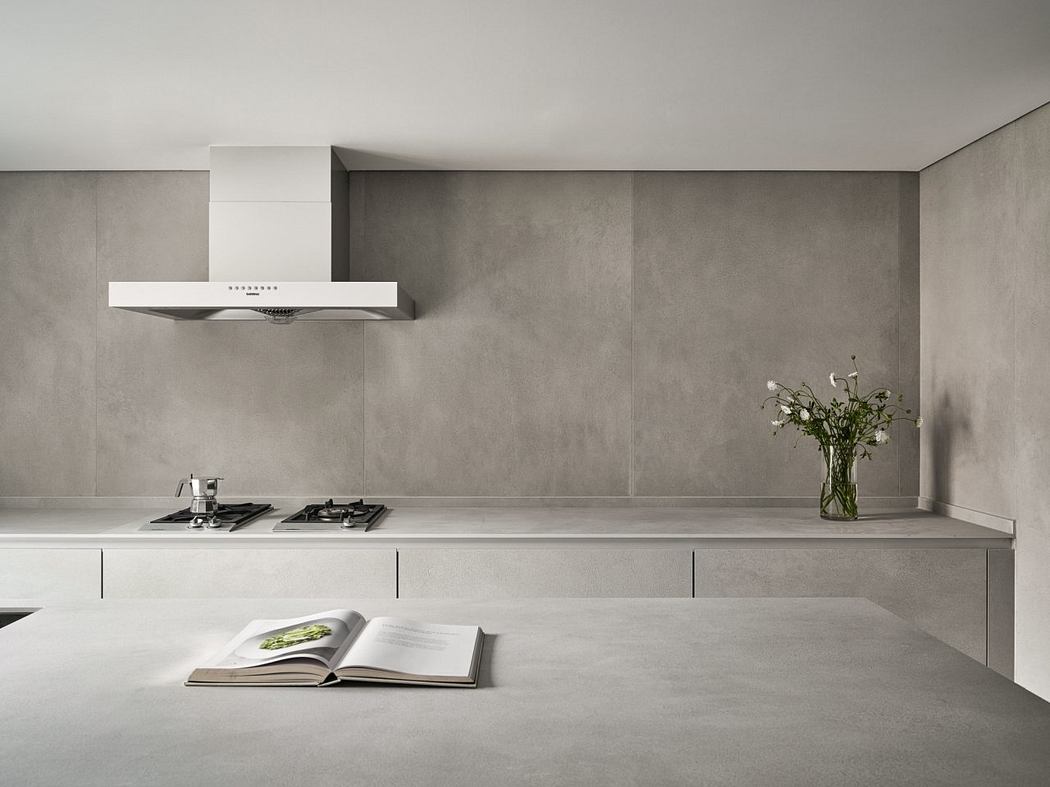 Minimalist kitchen with concrete walls, built-in appliances, and a vase of flowers.