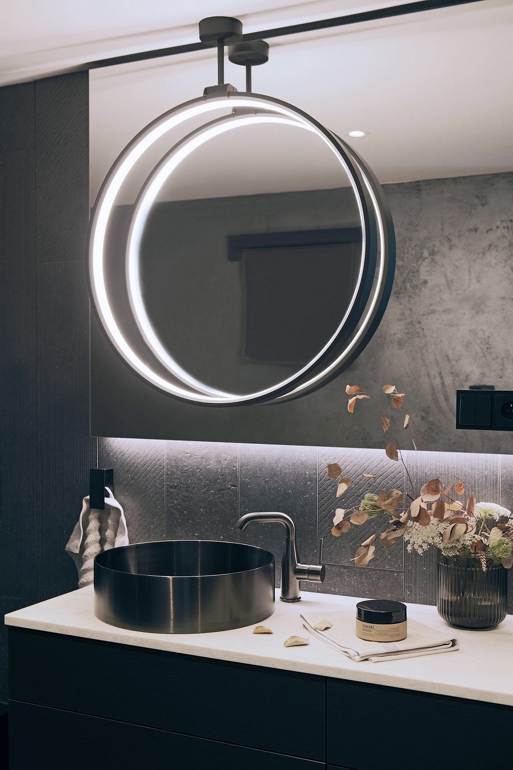 A modern bathroom design featuring a round backlit mirror, black vanity, and floral accents.