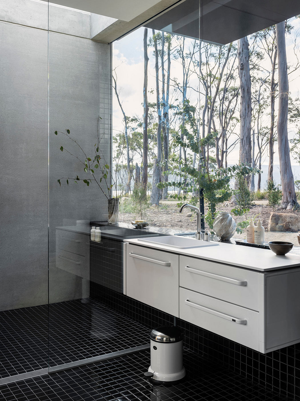 Contemporary bathroom with floor-to-ceiling windows, sleek white vanity, and black tiled floor.